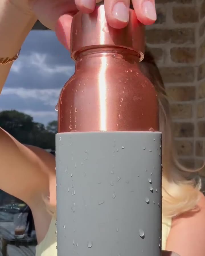Copper water bottle beaded with water, held up outdoors